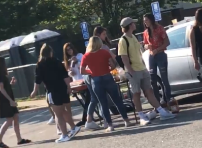 Students surrounding the food at the picnic in the parking lot.