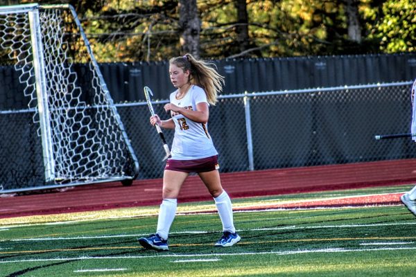 Junior Hailey Deptula walking up the  turf field during a game with a field hockey stick in hand. 