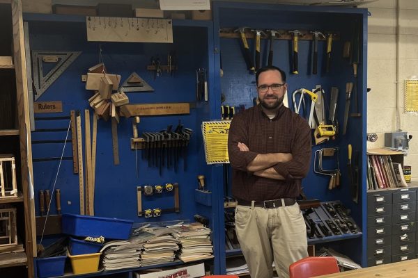 Tech education teacher and Bobcat Nation News advisor in front of the tool wall in the woodworking classroom.