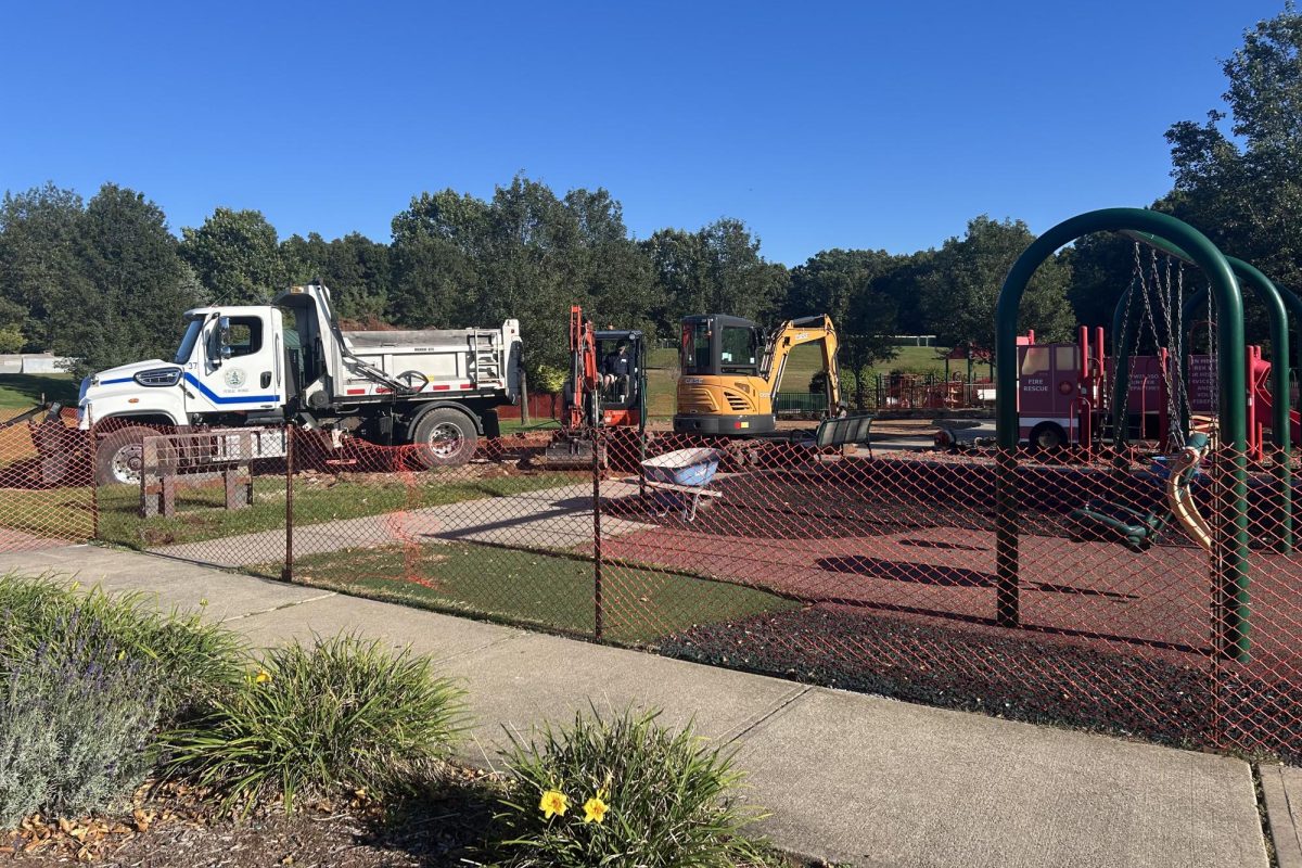 Construction vehicles and dump trucks work to expand playground area with new equipment.