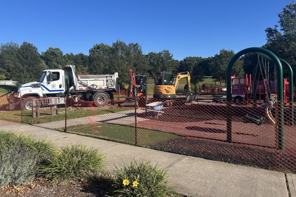Construction vehicles and dump trucks work to expand playground area with new equipment.
