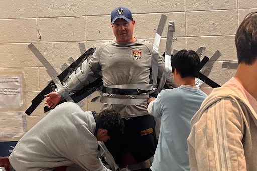 Students taping Mr. Carlson to the wall during 3rd lunch wave.