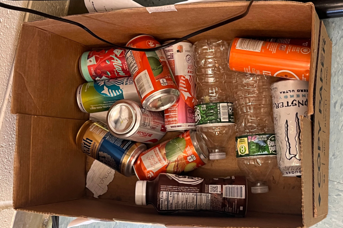 A recycling box in a classroom filled with several empty caffeinated drink cans.