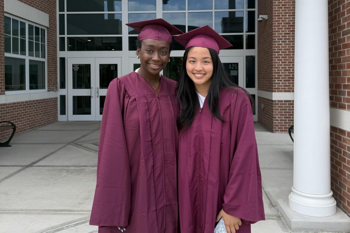 Seniors Elizabeth Sinclair and Audrey Zhang stand outside of Pleasant Valley Elementary School and take a photo in their cap and gown.